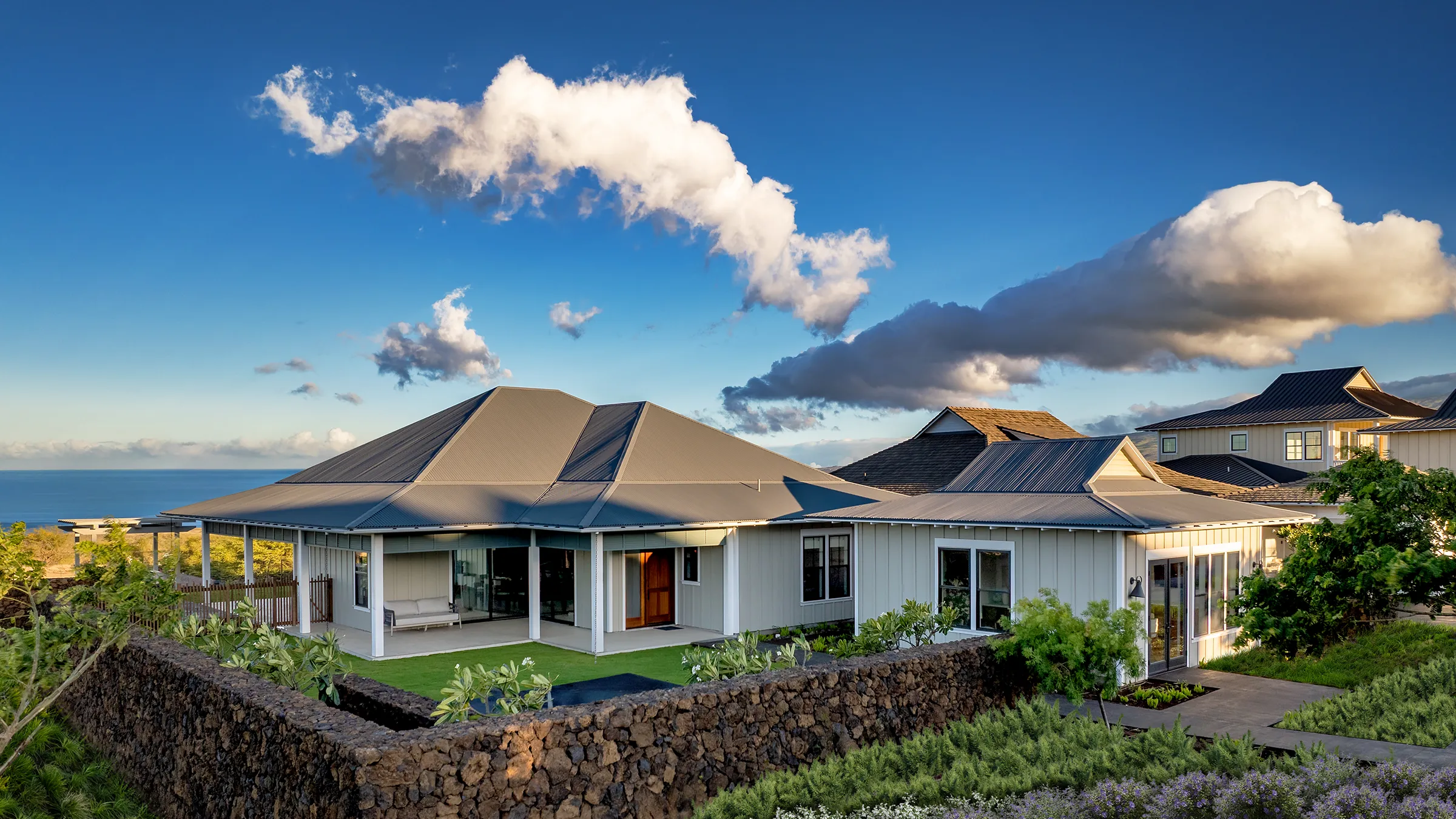 White house with a dark roof, surrounded by trees and plants.